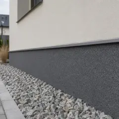 Ciemny, kamienny cokół wokół domu, otoczony żwirem, to świetny pomysł na wykończenie.