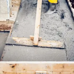 Wylewanie i wyrównywanie świeżego betonu w drewnianej formie za pomocą łaty.