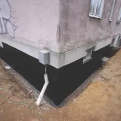 Trwa izolacja fundamentów w starym domu. Czarna membrana chroni ścianę przed wilgocią.