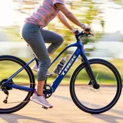 Kobieta na niebieskim rowerze elektrycznym Trek przemierza ścieżkę w słoneczny dzień.