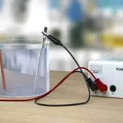 Eksperyment z elektrolizą wody: dwa elektrody zanurzone w wodzie, podłączone do zasilacza.