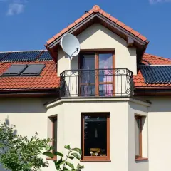 Fragment domu z wykusikiem, balkonem, oknami i kolektorami słonecznymi na dachu.