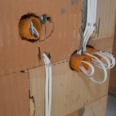 Pomarańczowe puszki elektryczne z przewodami w ścianie z cegły.