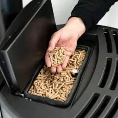 Dłoń wsypuje pellet do zasobnika pieca. Idealny piec na pellet do domu 120m2 to ekologiczne i ekonomiczne rozwiązanie.