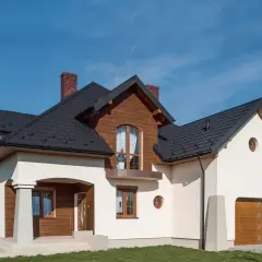 Nowoczesny dom z drewnianymi elementami i białym tynkiem. Solidny cokół na elewacji chroni budynek.