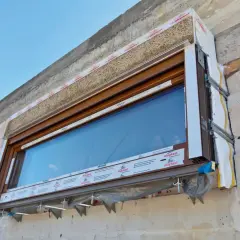 Fragment okna w trakcie ciepłego montażu, widoczna izolacja i elementy mocujące.