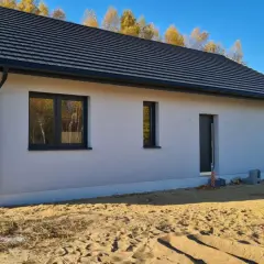 Nowy dom w stanie surowym zamkniętym z szarym dachem i oknami, otoczony piaskiem.