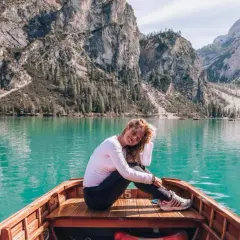 Kobieta w łodzi na tle turkusowego jeziora i górskiego krajobrazu Dolomitów.