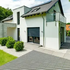 Nowoczesna elewacja wokół drzwi wejściowych z białym tynkiem, kamienną wiatą i zielenią.
