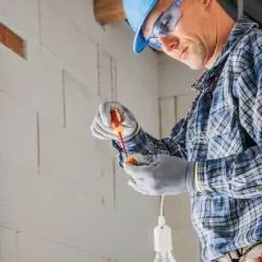 Elektryk w kasku i okularach montuje oprawkę żarówki. Dokładny koszt instalacji elektrycznej zależy od wielu czynników.