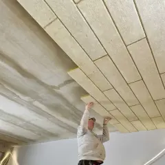 Mężczyzna montuje płyty izolacyjne na suficie betonowym.