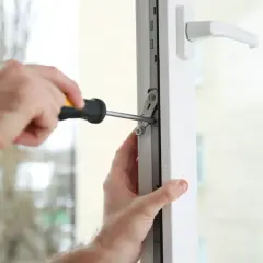 Regulacja drzwi balkonowych uchylnych. Ręce majsterkowicza dokręcają śrubę w mechanizmie okna.