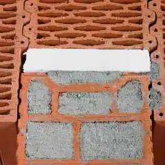 Zbliżenie na pustaki ceramiczne z zaprawą i białym elementem izolacyjnym.