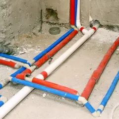 Skomplikowana instalacja wodna z rurami w kolorach czerwonym, niebieskim i białym, przygotowana do ukrycia w ścianie.