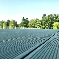 Szara deska kompozytowa tworzy nowoczesną nawierzchnię tarasu, otoczoną zielenią i jasnym niebem.