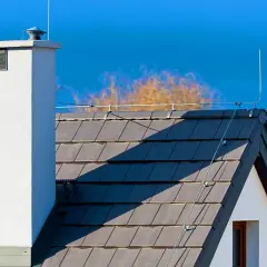 Fragment dachu z kominem i instalacją odgromową na tle błękitnego nieba.