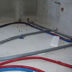 Na betonowej posadzce widać instalację wodną z czerwonych i niebieskich rur, które tworzą skomplikowany trojnik.