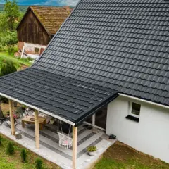 Nowy, ciemnoszary dach z blachodachówki nad tarasem i domem, otoczony zielenią.