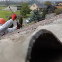 Pracownik w kombinezonie i kasku usuwa stare pokrycie dachowe z eternitu.