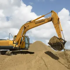 Żółta koparka Hyundai na placu budowy z piaskiem. Zastanawiasz się, ile kosztuje tona piasku?