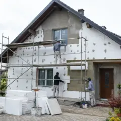Pracownicy na rusztowaniach ocieplają dom styropianem. Trwa praca nad elewacją, co wpływa na cenę ocieplenia za 1m2 robocizna.