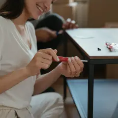 Kobieta z uśmiechem próbuje odkręcić wyrobioną śrubę krzyżakową, składając meble.