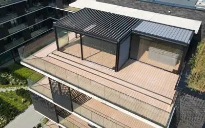 Nowoczesny taras na dachu z przeszklonym pawilonem i pergolą. Drewniana deska tarasowa i szklane balustrady tworzą elegancką przestrzeń.
