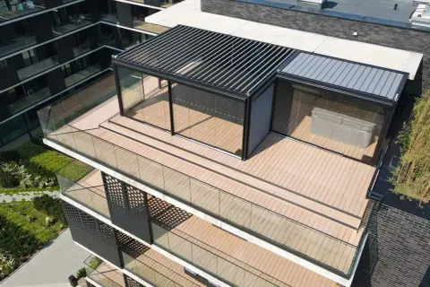 Nowoczesny taras na dachu z przeszklonym pawilonem i pergolą. Drewniana deska tarasowa i szklane balustrady tworzą elegancką przestrzeń.
