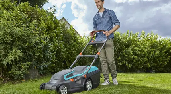 Mężczyzna z kosiarką elektryczną, która jest jedną z najlepszych kosiarek elektrycznych, dba o swój zielony trawnik.