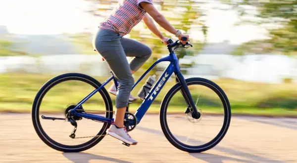Kobieta na niebieskim rowerze elektrycznym Trek przemierza ścieżkę w słoneczny dzień.