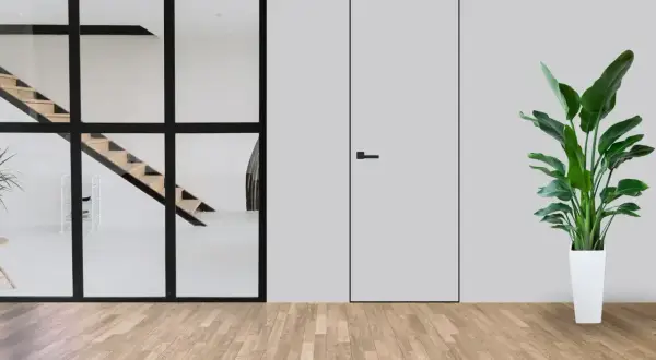Minimalistyczne wnętrze z widocznymi schodami za szklaną ścianą i dyskretnymi drzwiami ukrytymi w ścianie. Obok stoi duża roślina w białej donicy.