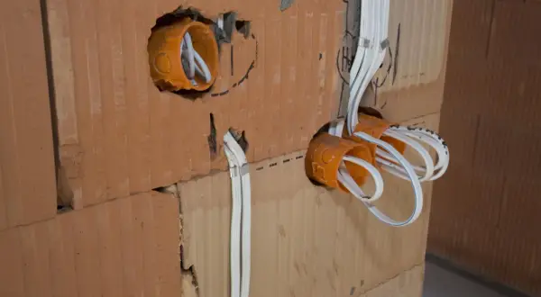 Pomarańczowe puszki elektryczne z przewodami w ścianie z cegły.