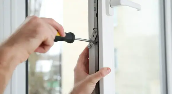 Regulacja drzwi balkonowych uchylnych. Ręce majsterkowicza dokręcają śrubę w mechanizmie okna.