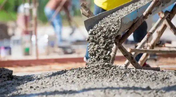 Betoniarka wylewa świeży beton. Pracownicy na budowie dbają o odpowiednią ilość cementu na kubik betonu, by zapewnić trwałość konstrukcji.