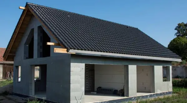 Dom w stanie surowym otwartym, z dachem pokrytym czarną dachówką. Ściany z bloczków betonowych, bez okien i drzwi.