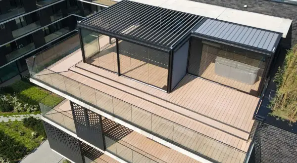 Nowoczesny taras na dachu z przeszklonym pawilonem i pergolą. Drewniana deska tarasowa i szklane balustrady tworzą elegancką przestrzeń.