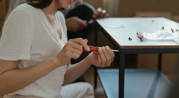 Kobieta z uśmiechem próbuje odkręcić wyrobioną śrubę krzyżakową, składając meble.
