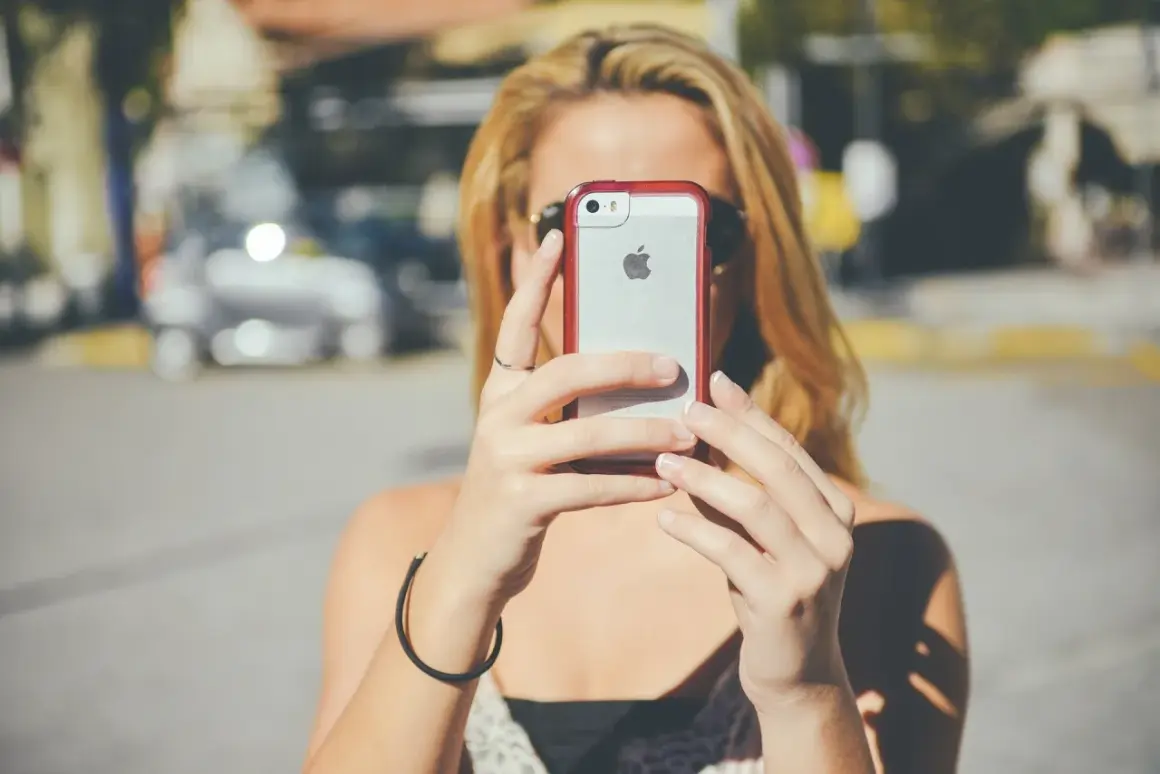 Kobieta z blond włosami trzyma iPhone'a, być może wykonując twardy reset.