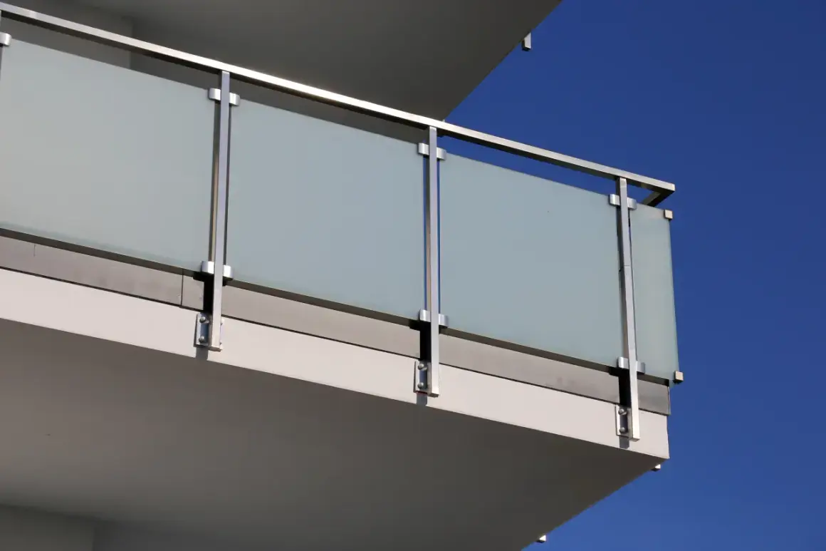 Nowoczesne mocowanie balustrady od czoła z matowego szkła i stali nierdzewnej na tle błękitnego nieba.