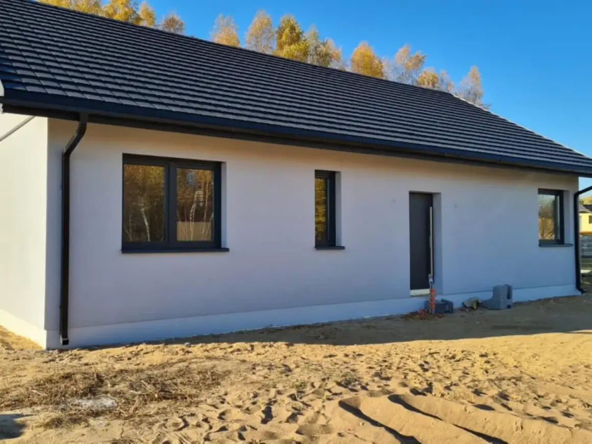 Nowy dom w stanie surowym zamkniętym z szarym dachem i oknami, otoczony piaskiem.