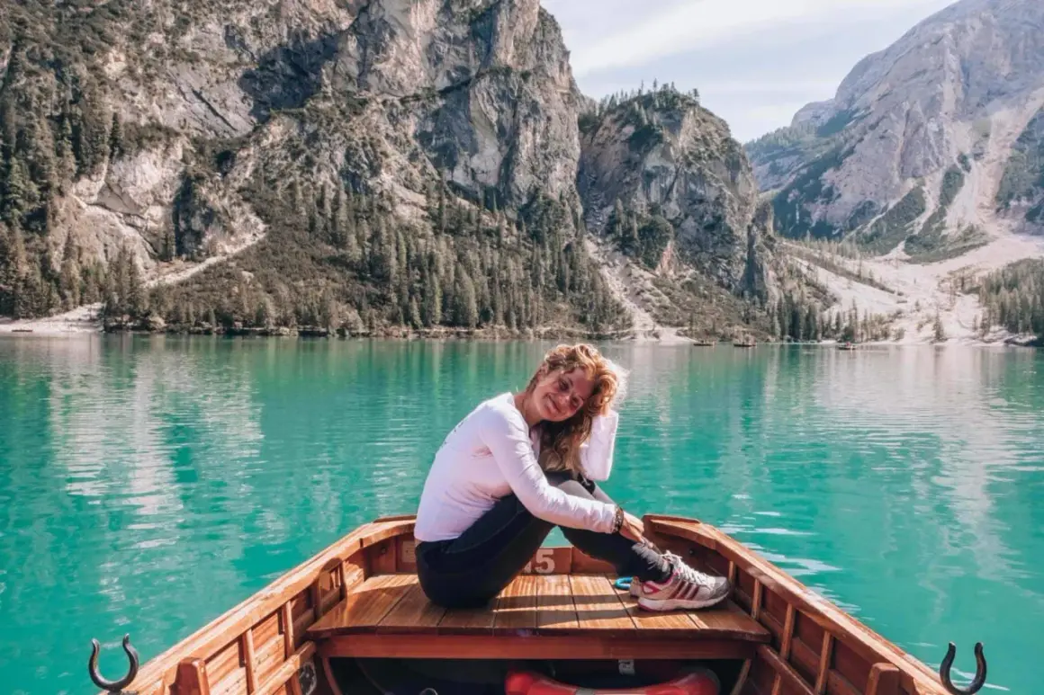 Kobieta w łodzi na tle turkusowego jeziora i górskiego krajobrazu Dolomitów.