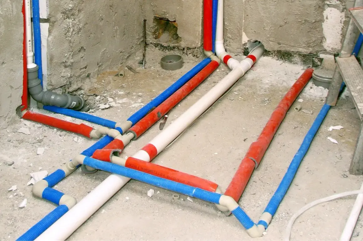 Skomplikowana instalacja wodna z rurami w kolorach czerwonym, niebieskim i białym, przygotowana do ukrycia w ścianie.