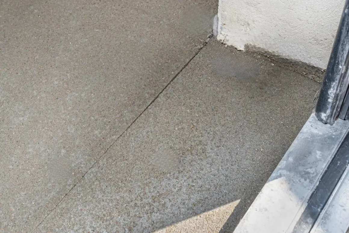 Szara betonowa posadzka z widoczną linią dylatacji biegnącą w kierunku narożnika budynku.