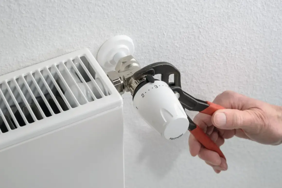 Dłoń z kombinerkami dokręca termostat grzejnika. Regulacja temperatury w domu to klucz do komfortu.