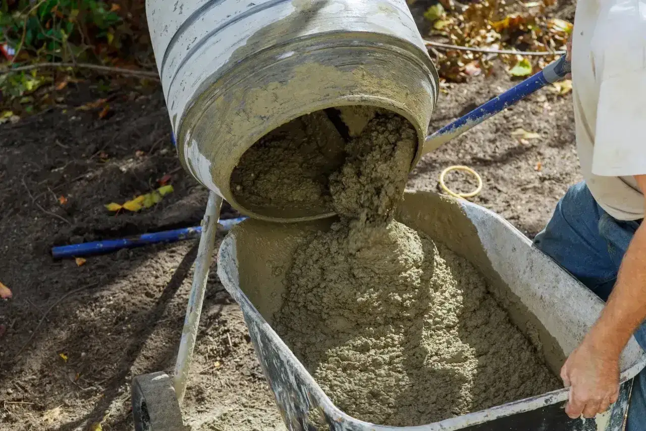 Mieszanie betonu w betoniarce. Wylewanie świeżej masy do taczki. Kluczowe jest właściwe dobranie, ile cementu na kubik betonu, by uzyskać trwałą konstrukcję.