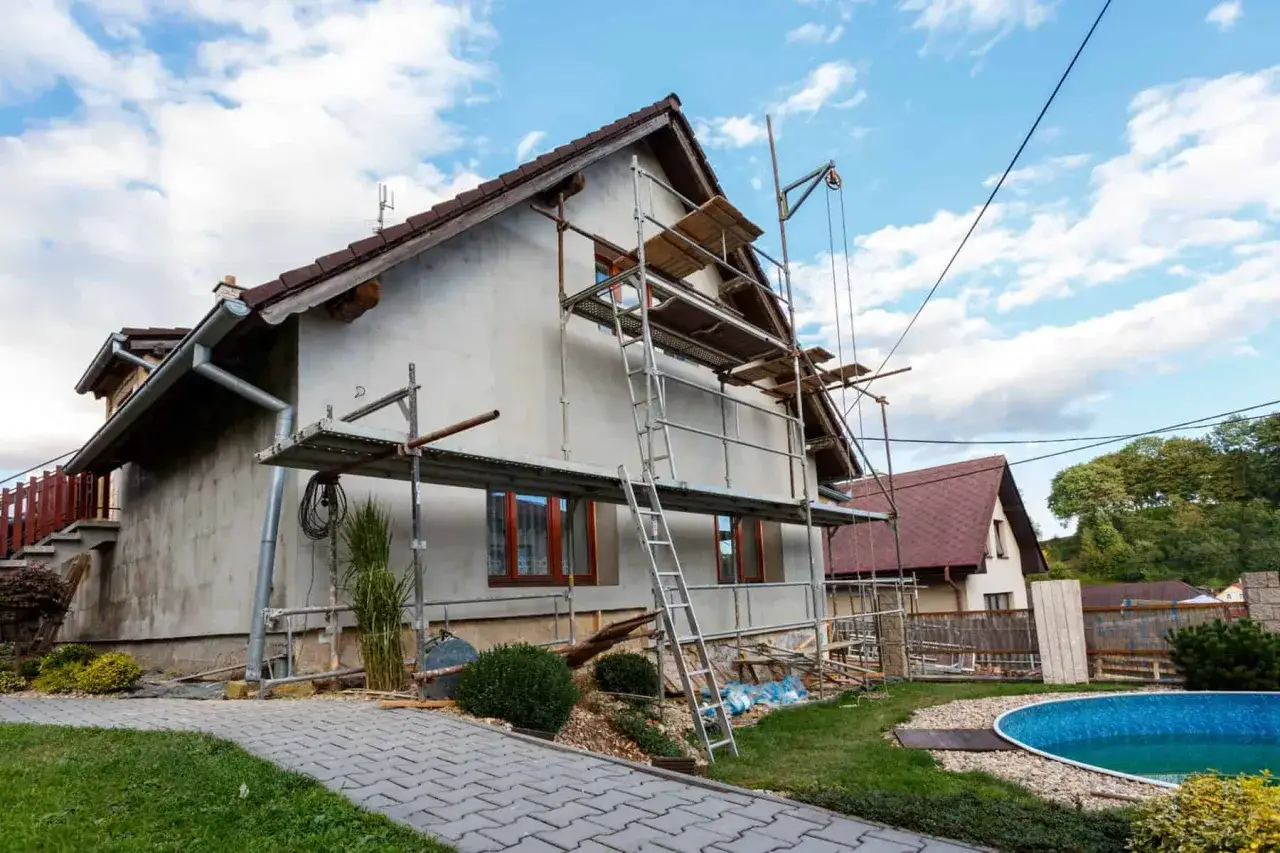 Rozbudowa domu w toku. Rusztowania otaczają budynek, a w tle widać basen.