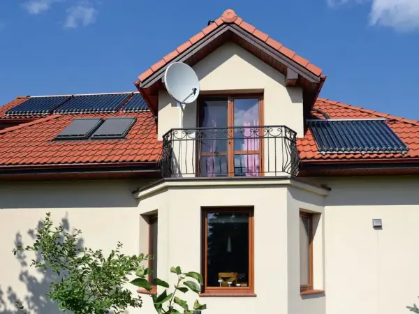 Fragment domu z wykusikiem, balkonem, oknami i kolektorami słonecznymi na dachu.