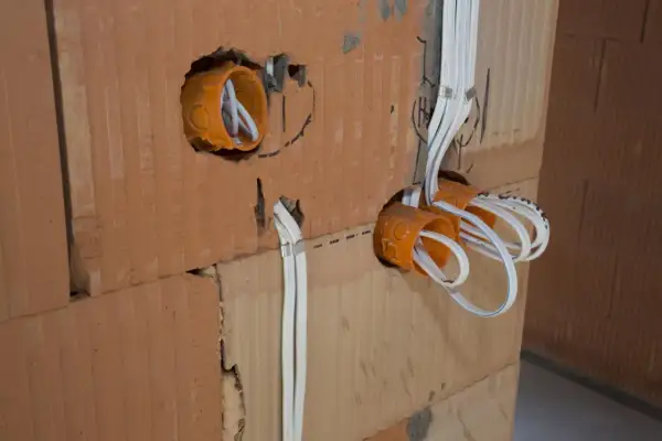 Pomarańczowe puszki elektryczne z przewodami w ścianie z cegły.