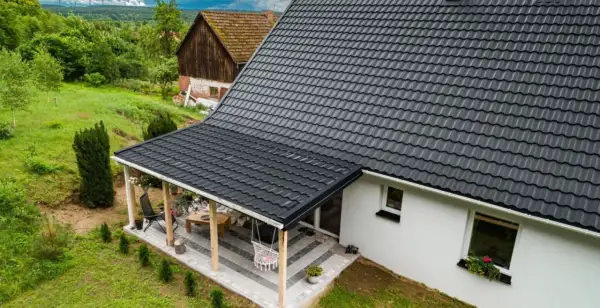 Nowy, ciemnoszary dach z blachodachówki nad tarasem i domem, otoczony zielenią.