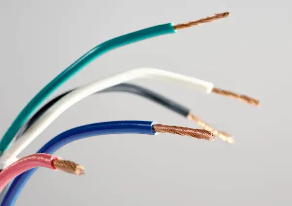Pięć przewodów elektrycznych w różnych kolorach: zielonym, białym, czarnym, niebieskim i różowym, odsłaniających miedziane żyły. Różnorodność kolorów faz ułatwia identyfikację.